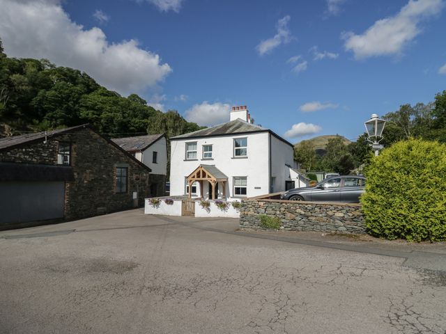 A white two-story house with a wooden porch and flower boxes next to stone buildings and a parked car at Briery House in Keswick