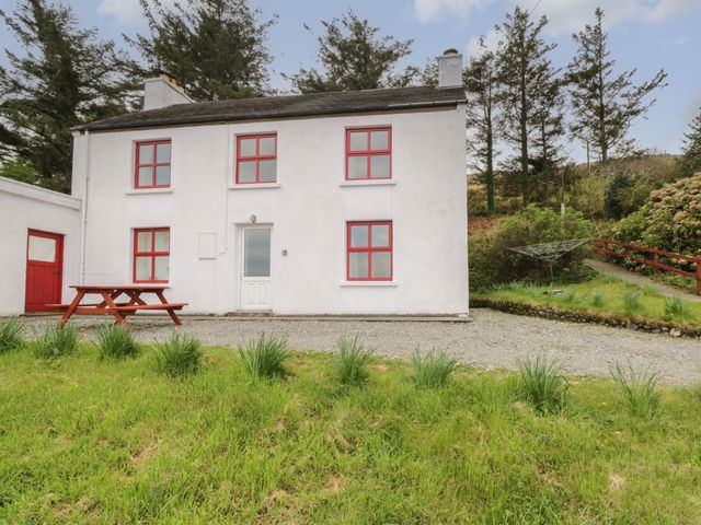 A white two-story house with red window frames and a red door a wooden picnic table and grassy lawn at Sea View House in Tully County Galway