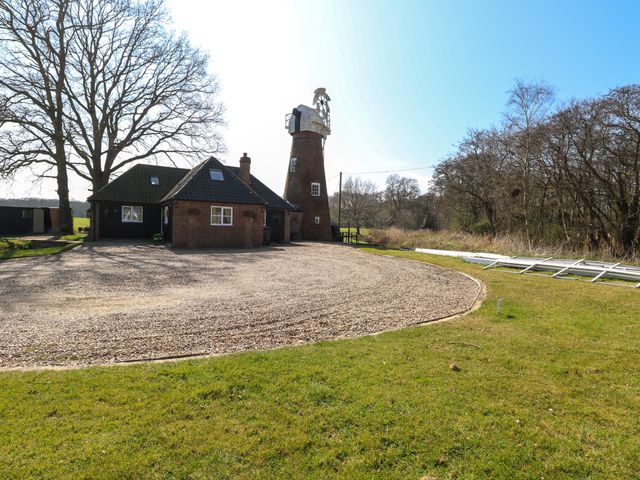 A house with an attached windmill structure surrounded by grass and trees at Wayford Mill in Wayford