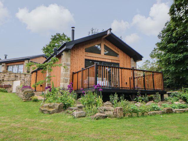 A wooden house with a deck and garden with flowers in front at The Bothy Riding Hills Riding Mill near Corbridge