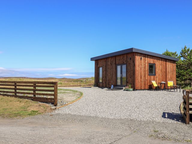 A small wooden cabin with a gravel driveway and two yellow chairs outside at The Wheelhouse in Grimsay near Balivanich