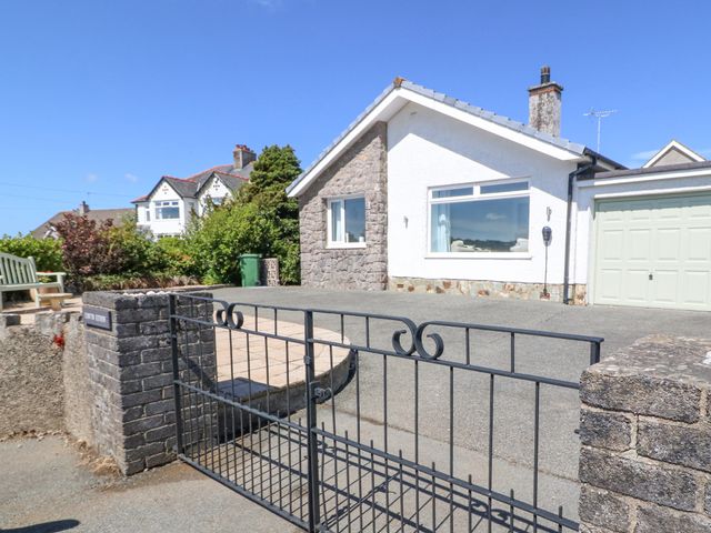 A driveway with a metal gate leading to a house with stone and white exterior walls and a garage at Llwyn Eithin in Benllech