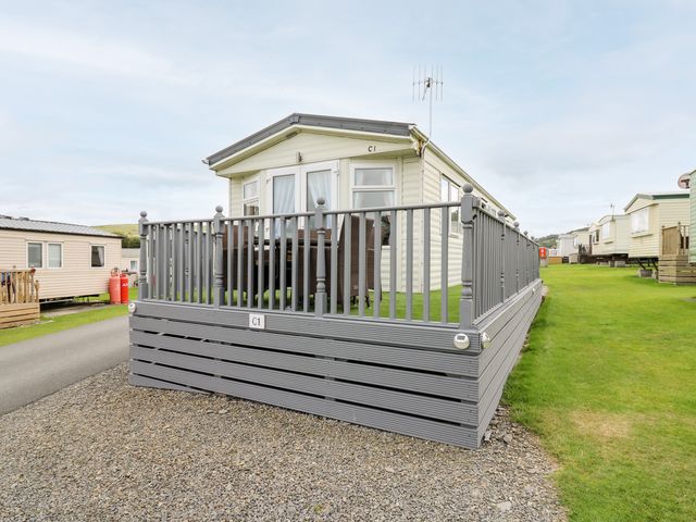 A static caravan with a grey deck and railing on a gravel and grass plot at Bryn Vista in Aberystwyth