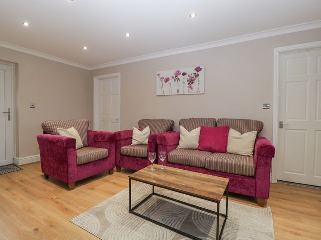 A living room with pink and striped sofas a wooden coffee table with two wine glasses and a floral wall painting at Myrtle Cottage in St Brides-Super-Ely