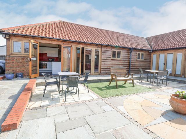 An outdoor patio area with tables and chairs a wooden bench and a tiled floor at 5a Hideaways in Hunstanton