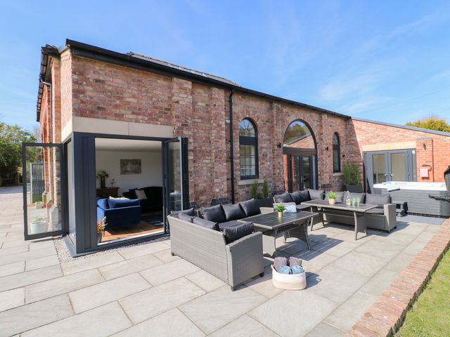An outdoor patio with grey wicker sofas and tables next to a brick building with arched windows at The Old Pump House in Annesley near Kirkby-In-Ashfield