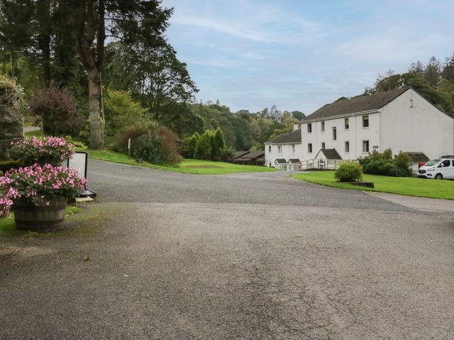 A driveway leading to a white building with cars and flower pots in a green area at Apartment 3 in Keswick