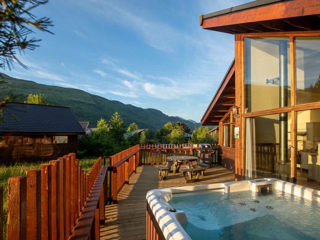 A wooden deck with a hot tub picnic table and barbecue grill overlooking mountains at Ardgartan Argyll Golden Oak Lochside Ardgartan Loch Long