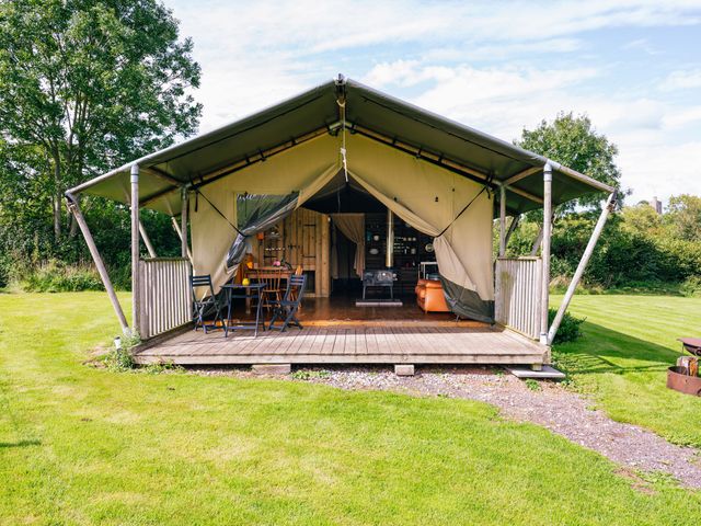 An outdoor tent with a wooden deck table and chairs surrounded by grass and trees at Oak Stockland near Dalwood