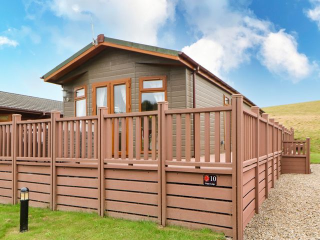 A wooden lodge with a fenced deck and gravel path outside at 10 Poppy Lodge in Tunstall near Catterick North Yorkshire