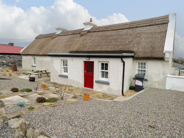 A cottage with a thatched roof red door white walls gravel driveway and a picnic bench at Freemans Cottage in Enniscrone County Sligo