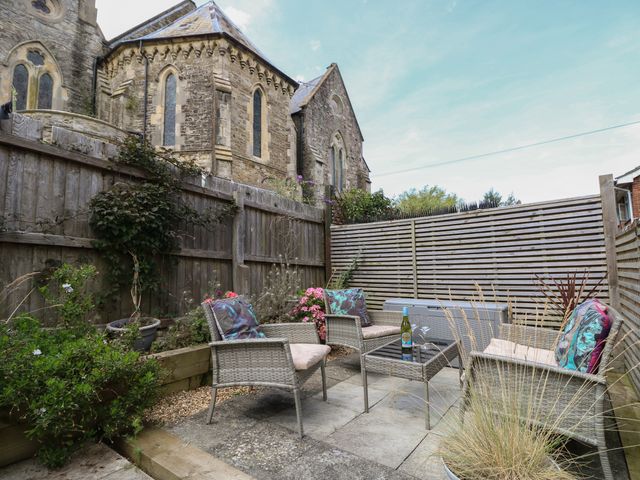 A small outdoor patio with three wicker chairs around a glass coffee table and a wooden fence at Sundowners in Ryde