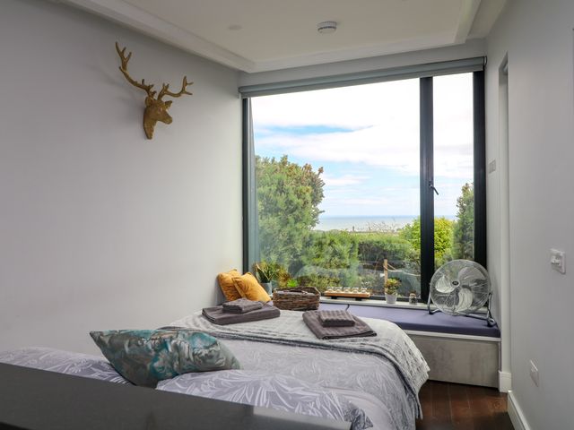 A bedroom with a bed towels pillows a fan and large window with outside view at Stormchaser Tara Hill near Ballymoney County Wexford