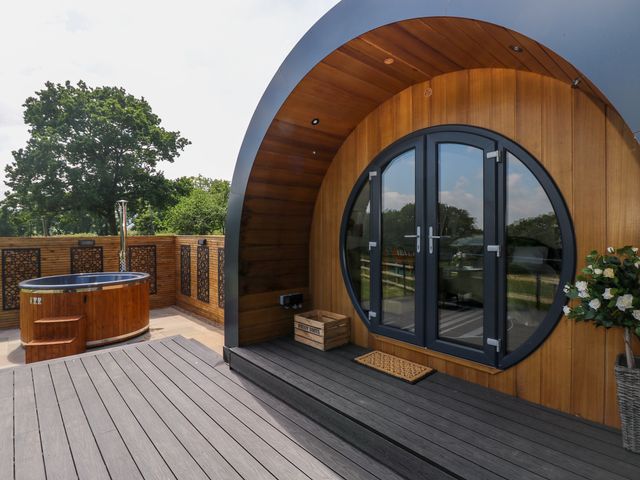 An outdoor deck with a round wooden hot tub and circular framed glass doors on a wood-paneled pod at Roselea Luxury Pod Lodge in Llanddarog