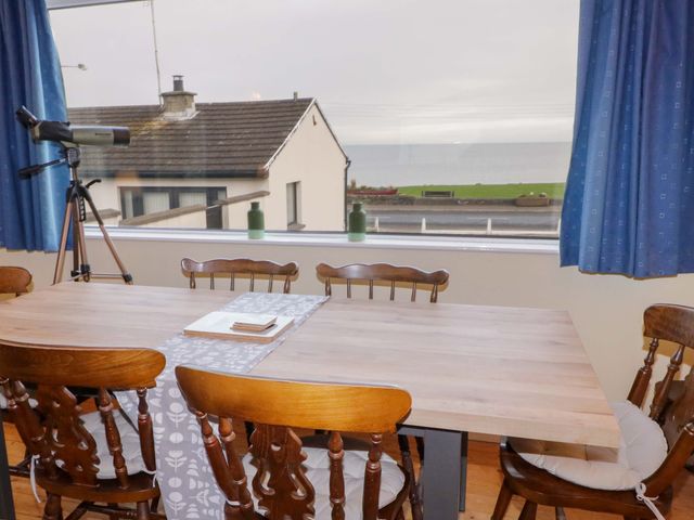 A dining area with wooden chairs and table near a large window with a telescope and blue curtains at Dee by the Sea in Donaghadee