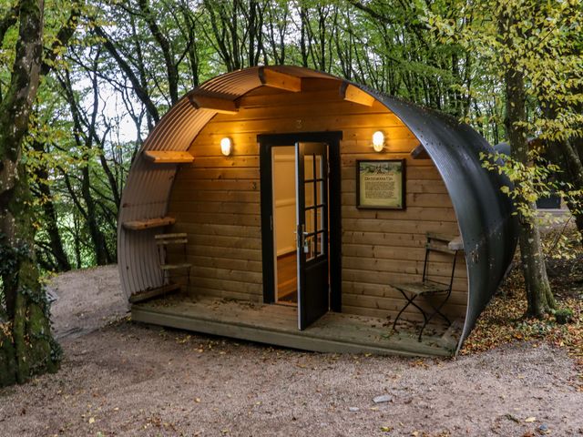 A small wooden pod with a curved metal roof in a wooded area with two chairs on the porch at Ballybeg Pod 3 in Tinahely County Wicklow
