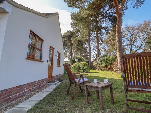 A garden with wooden chairs and a small table with two mugs outside a white house at West End in Martlesham Village