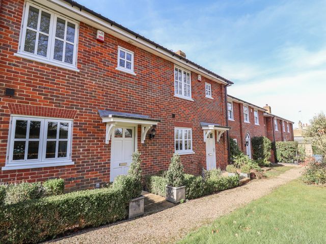 A row of red brick townhouses with white doors and windows along a gravel path with trimmed hedges and grass