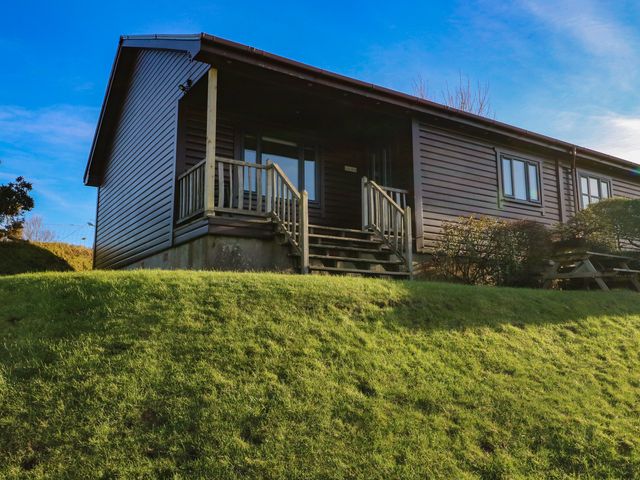 A wooden cabin with a small staircase and railing on a grassy hill at Glen Mhor Lodge in Arisaig