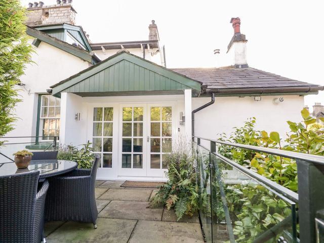 A patio with a round glass table and wicker chairs outside a white building with glass doors at The Bolt Hole in Kendal