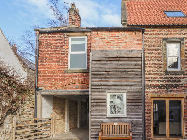Exterior of a brick and wood house with windows a wooden bench and a gate at Seafield Coach House in Alnmouth