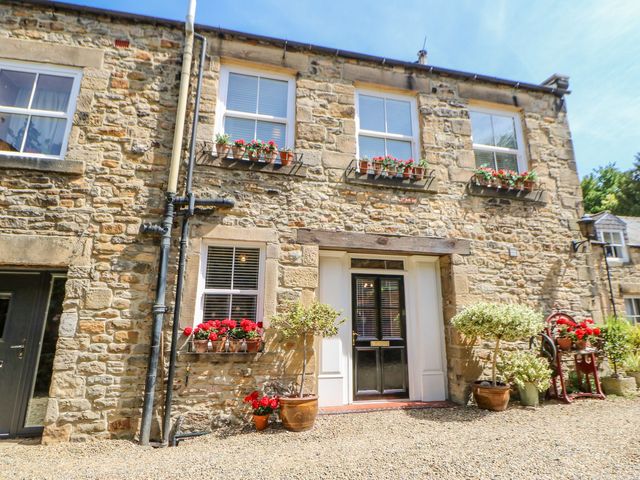 Stone house exterior with black front door and flower pots on windowsills and ground at Shaftoe Mews in Haydon Bridge