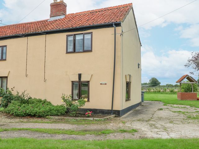 The exterior of a semi detached house with beige walls red tiled roof garden and a brick well in the yard at 2 Stud Cottage in Hainford near Buxton Norfolk
