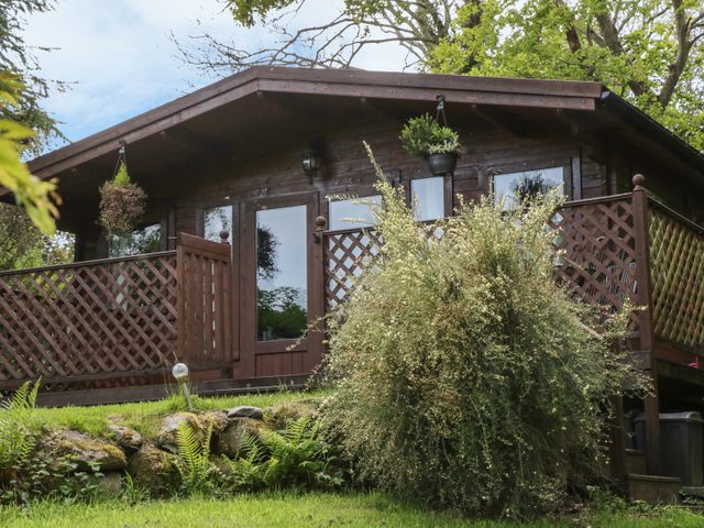 A wooden cabin with a porch and lattice railing surrounded by greenery at Y Caban in Llechwedd The Conwy Valley