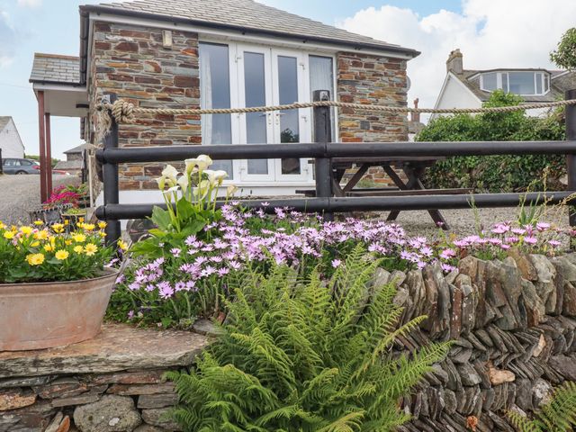 A stone cottage with a wooden fence and flowers in front at Sunset Cottage in Bossiney near Tintagel