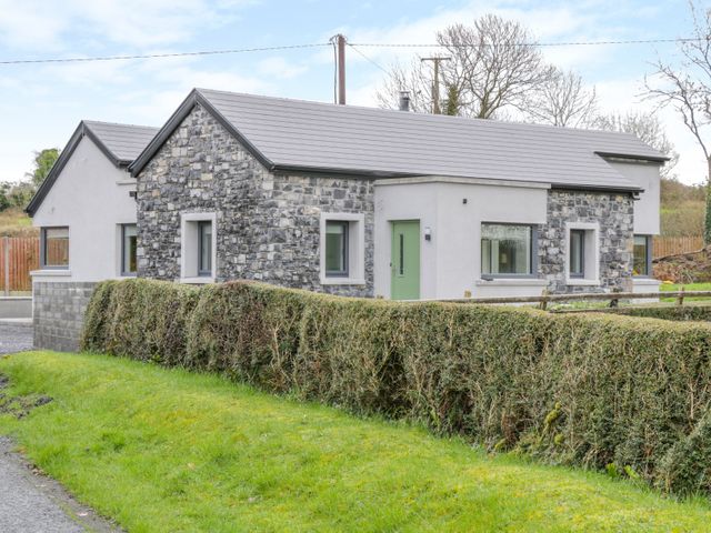 A single story house with stone and white exterior walls and green door behind a trimmed hedge at River Dale in Sligo Town