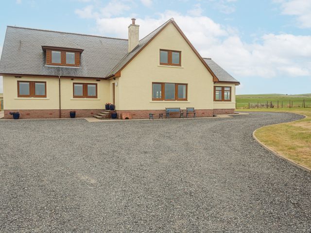 A house with multiple windows and a gravel driveway with blue benches outside Corsewall Castle Farm Lodges in Kirkcolm