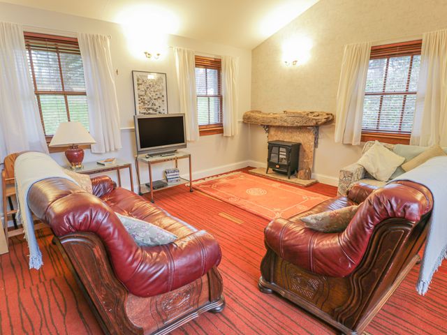 A living room with two red leather sofas a television on a stand and a fireplace at Mercat Cottage in Cockenzie and Port Seton near Edinburgh