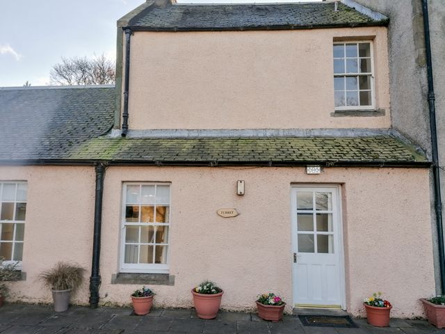 The exterior of a two-story house with a white door, three windows, flower pots, and a sign reading turret at Turret Cottage in Cockenzie and Port Seton