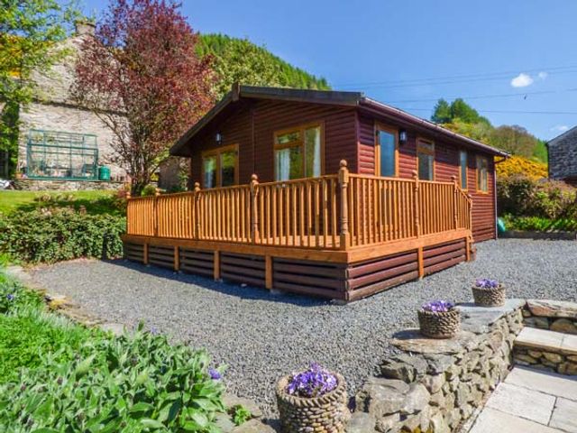 A wooden cabin with a raised deck and potted flowers on a stone wall at North Lodge in Kendal