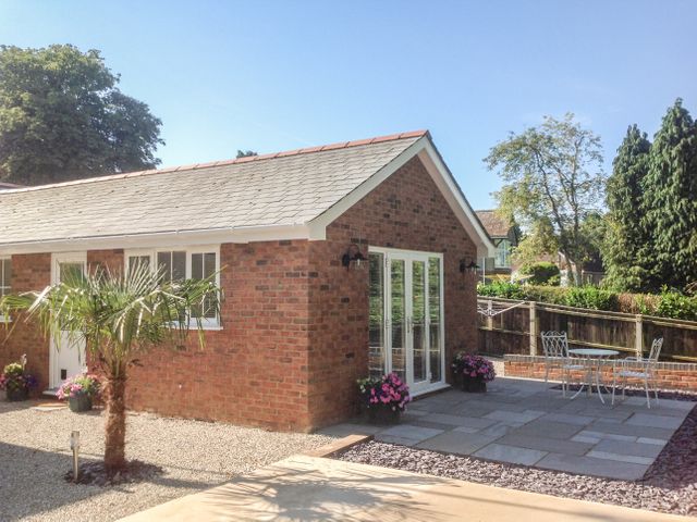 A small brick house with a tiled roof and a patio area with a table and chairs surrounded by plants and trees at The Hideaway in Verwood
