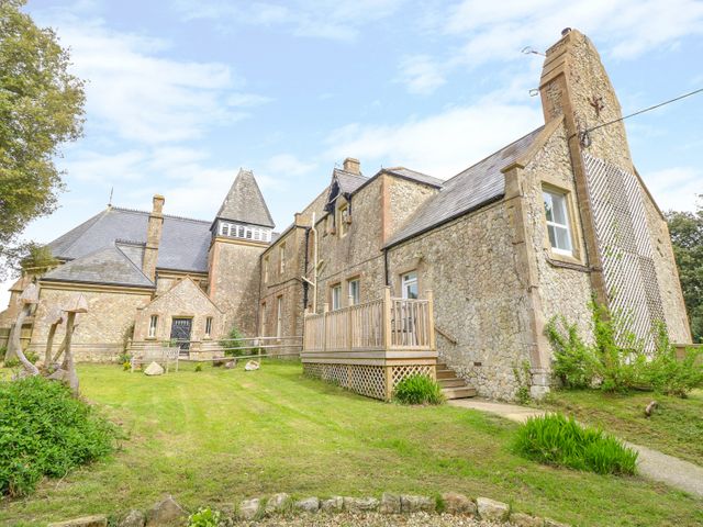 The exterior of a stone building with slate roofs and a wooden deck surrounded by grass and trees at The Old Kitchens in Totland Bay