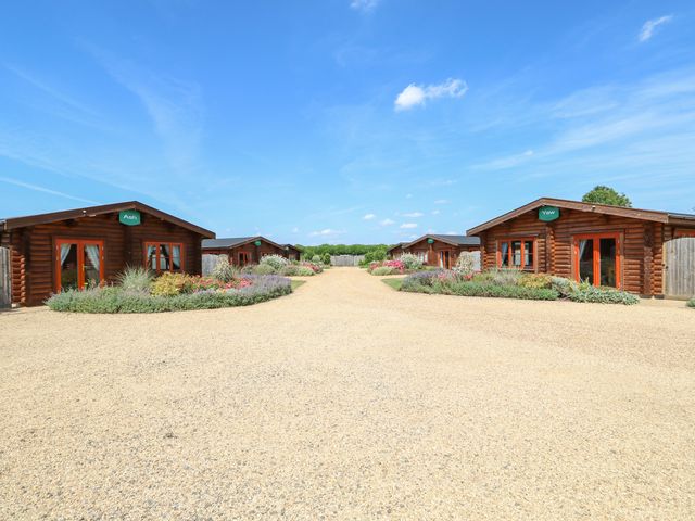 A gravel driveway between wooden cabins with flower beds at Willow Lodge in Greetham Rutland