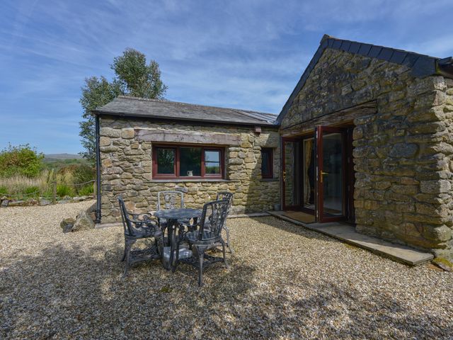 An outdoor patio area with a metal table and four chairs beside a stone building at Buster Barn in Sampford Spiney near Tavistock
