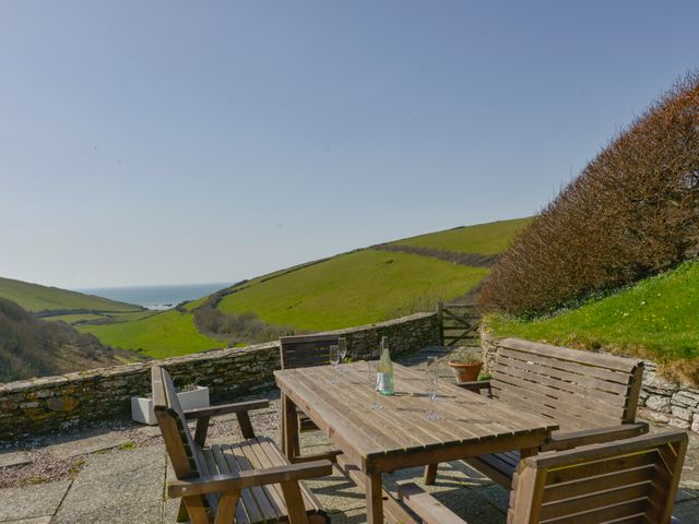 An outdoor patio with a wooden table and chairs overlooking green hills and the sea at Ayrmer House in Ringmore