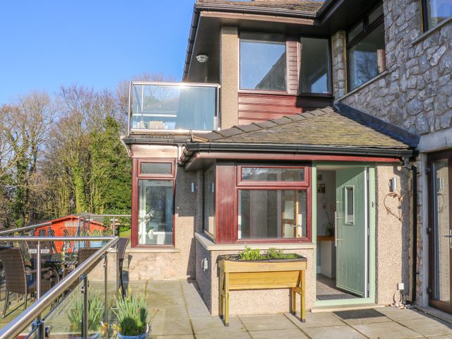 A patio with a glass railing table and chairs and a door leading inside a stone and pebble dash house at Shady Bowers in Arnside