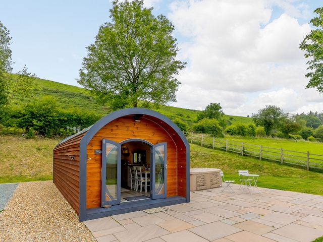 A wooden pod with glass doors open showing a dining area outside a hot tub on a stone patio at Stiperstones Pod in White Grit near Chirbury
