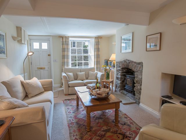 A living room with sofas a wooden coffee table a stone fireplace and a window with curtains at Jot Cottage in Salcombe