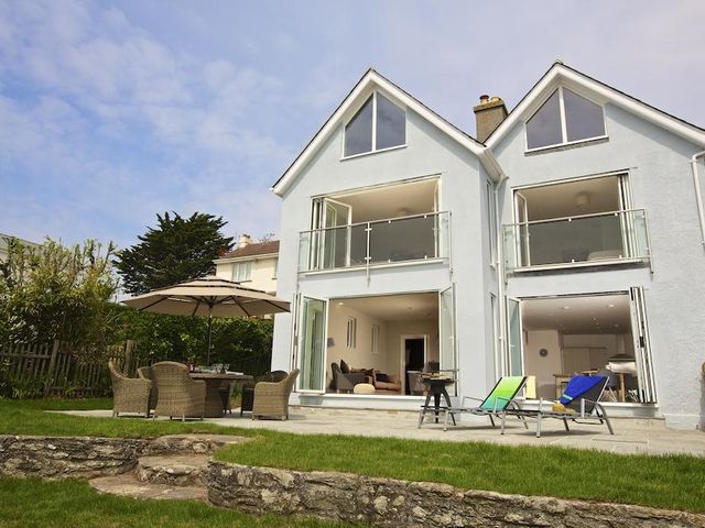 A white two story house with open glass doors leading to a patio with outdoor furniture and sun loungers at Sundowners Salcombe