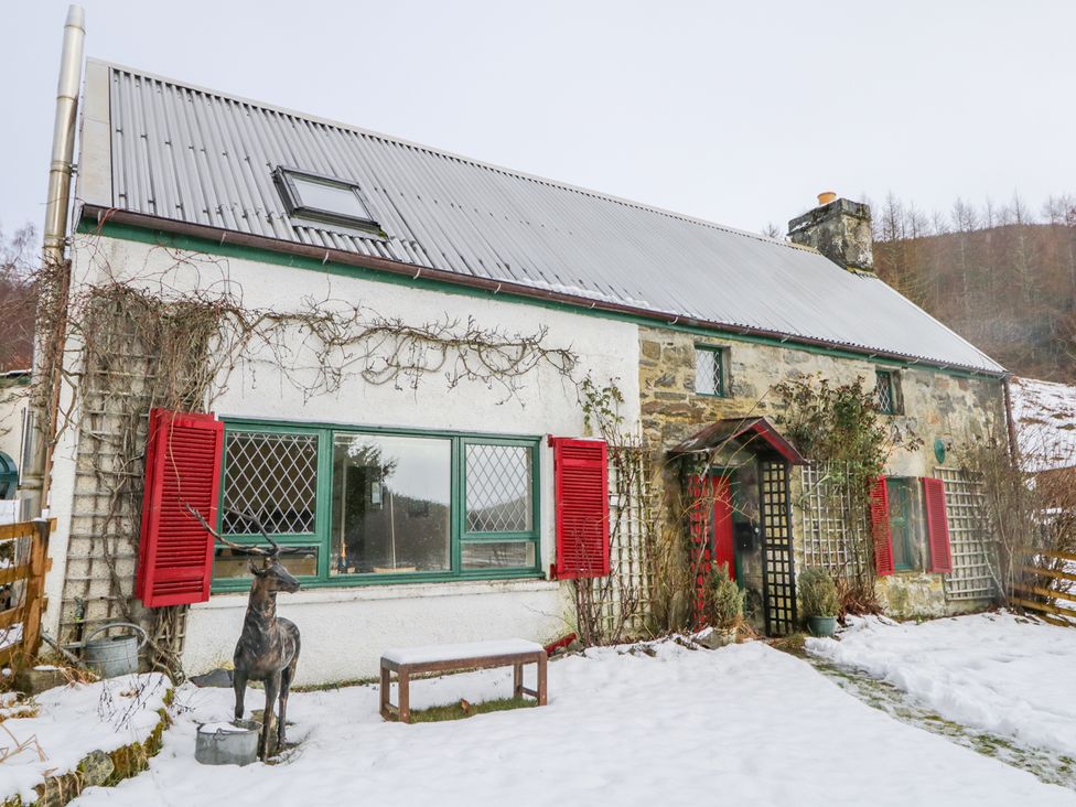 A stone and white exterior cottage with red shutters and a metal roof in a snowy yard at The Old Mill in Cannich