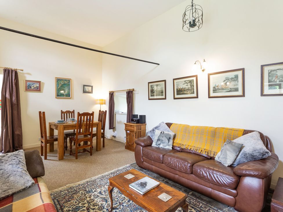 A living room with a brown leather sofa, wooden dining table with chairs, framed pictures on walls, and a coffee table at The Old Mill in Cannich
