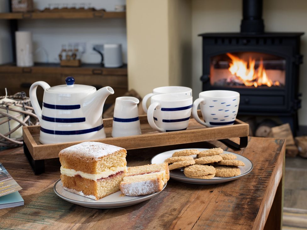 A wooden table with a teapot and cups on a tray and plates with cake and biscuits by a fireplace at Lambs Lodge in Bamburgh