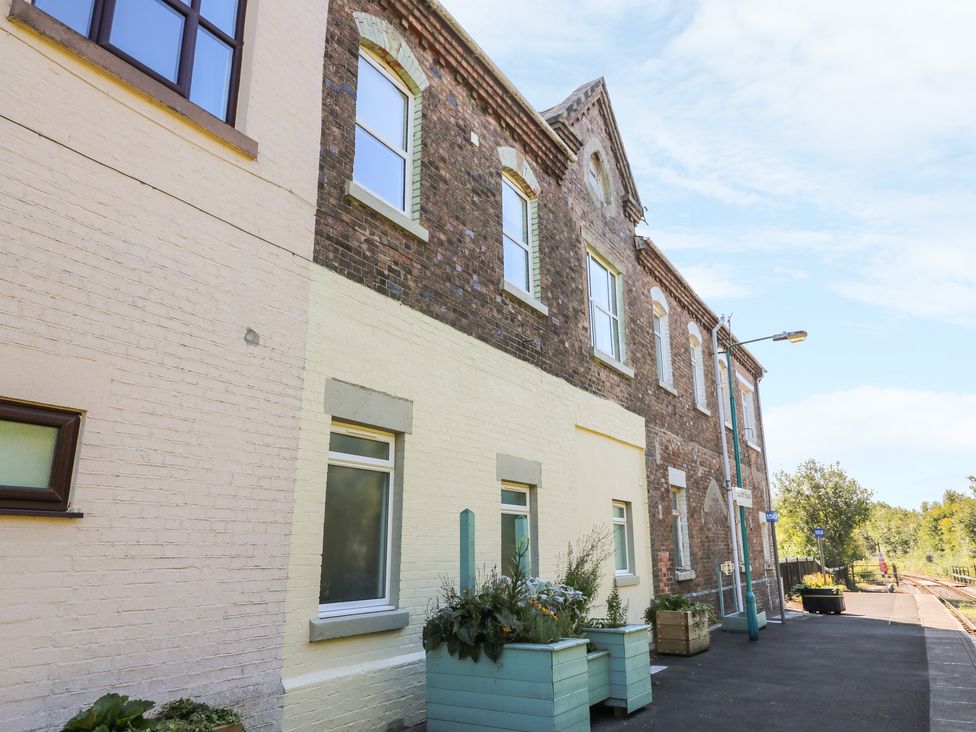 A brick building with windows and planters along a sidewalk by a railway track at Ty'r Orsaf in Builth Wells