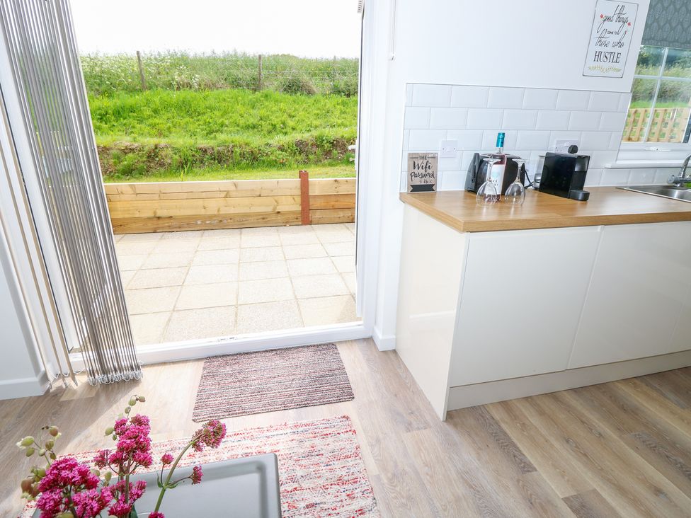 A kitchen area with a wooden countertop, glassware, a coffee machine and a door opening to a tiled patio with grass beyond at 6 Yarmouth Cottages Norton Green near Freshwater