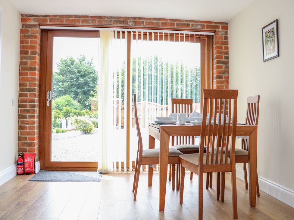 A dining area with a wooden table and four chairs near glass sliding door with vertical blinds at Thistledown Cottage in Chidham near Bosham