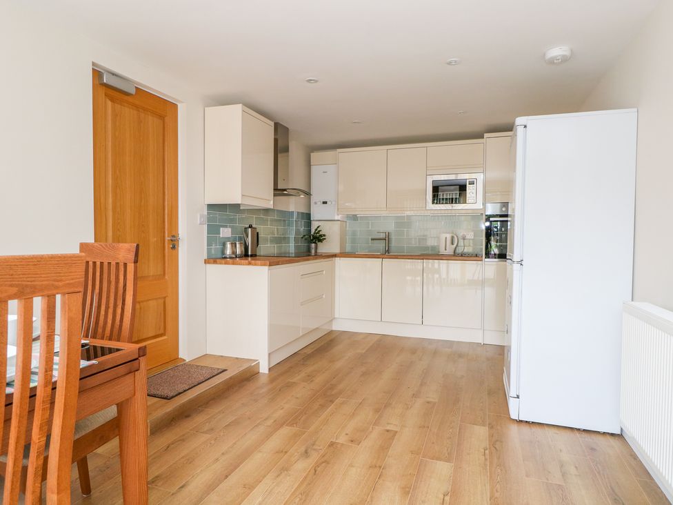 A kitchen with wooden floor white cabinets white fridge and wooden dining table and chairs at Thistledown Cottage in Chidham near Bosham